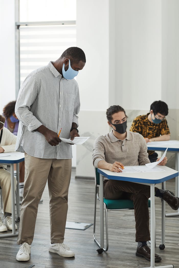 Students and teacher in masks during a classroom exam amid COVID-19 precautions.